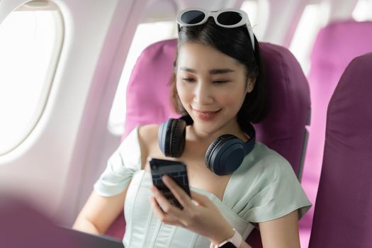 Joyful asian woman sits in the airplane and using mobile phone while go to travel.