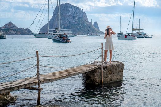 Brunette woman with hat and light beige dress on Ibiza pier