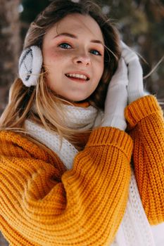 Teen blonde in a yellow sweater outside in winter. A teenage girl on a walk in winter clothes in a snowy forest.
