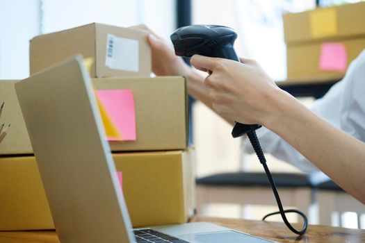 Female small online business owner holding scanner scanning parcel barcode tag before shipment at workplace. Woman selling products online, scanning parcel barcode. Online business concept.