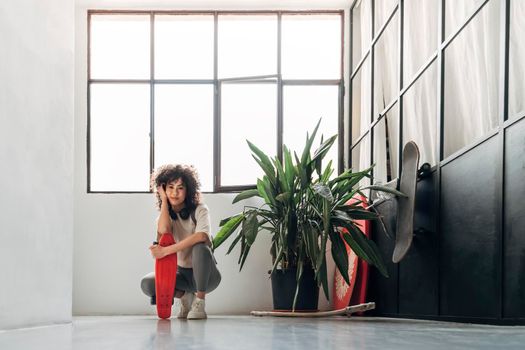 Young multiracial woman crouching down with skateboard looking at camera. Copy space. Lifestyle concept.