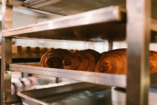 Production of delicious buns. Family bakery. Hot croissants on a metal tray. Fresh bakery. Rack with baked croissants.