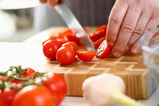 Closeup of man hand cutting tomato on cutting board at home. Cooking and healthy vegetarian food concept