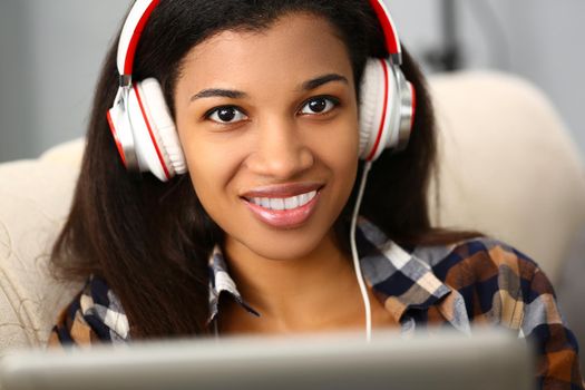 Smiling woman with headphones on sofa and listening to music. Application for watching movies or learning foreign languages