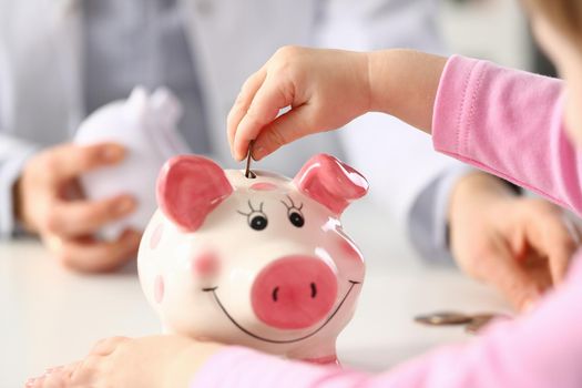 Child hand put a money coin in piggy bank to save money wealth. Family health insurance and budget