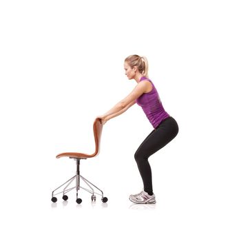 Crouching to strengthen her core. A beautiful young woman wearing gym clothes and crouching down while using a chair for support against a white background