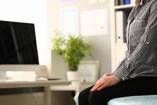 Closeup of young woman sitting on couch with folded hands on knees. Thoughtful woman waiting for important news in clinic and difficult decision about treatment of diseases