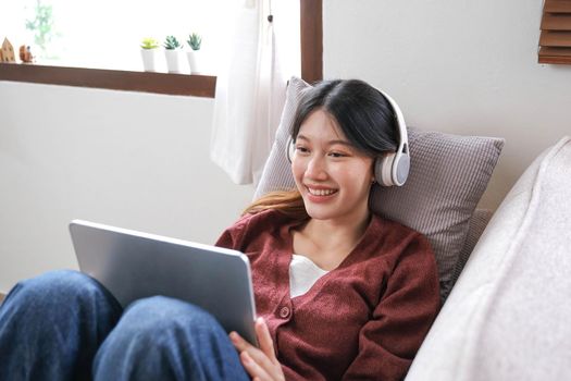 Attractive smiling young woman using tablet and listen music on sofa at home. lifestyle concept..