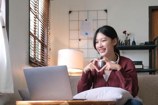 Attractive smiling young woman video call by laptop on sofa at home. lifestyle concept.