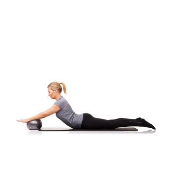 Working out forms part of her daily routine. A young woman pushing an exercise ball down while isolated on a white background
