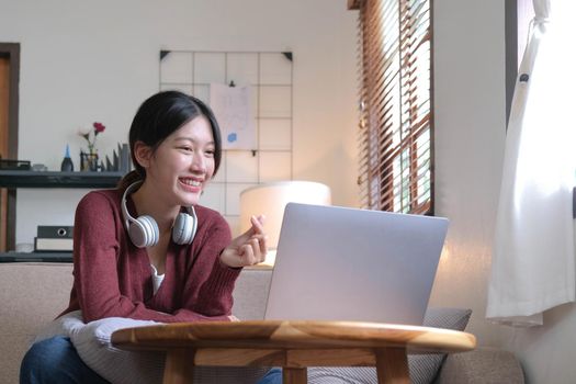 Attractive smiling young woman video call by laptop on sofa at home. lifestyle concept.