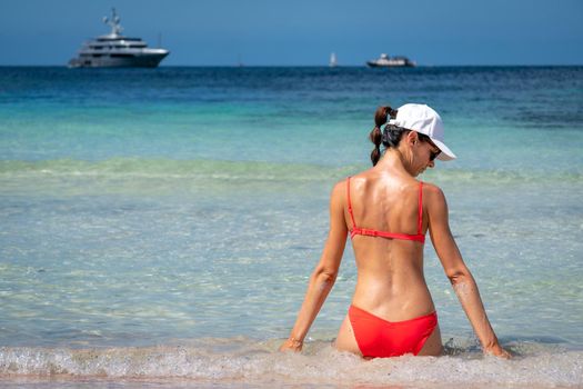 Brunette woman with coral bikini and cap posing on the beach