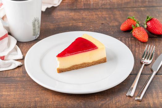 Delicious strawberry cheesecake with coffee next to it on wooden table