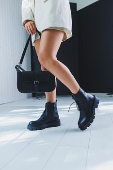 Fashionable leather boots on a woman's leg, close-up, fashionable. Leather bag in female hands.