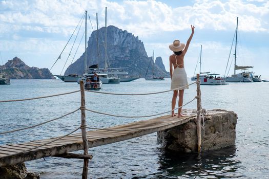 Brunette woman with hat and light beige dress on Ibiza pier