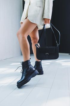 Fashionable leather boots on a woman's leg, close-up, fashionable. Leather bag in female hands.