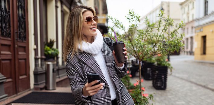 woman Tourist walks around the city sightseeing with a cup of coffee and a mobile phone.