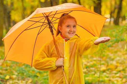 Happy child in the rain. Funny kid playing outdoors and catching rain drops in Autumn park