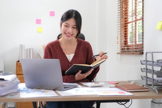 Portrait of an Asian young Female working on a laptop computer in home, Asian woman happy hold notebook and pen at home.