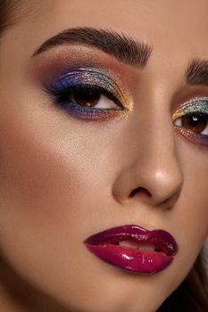 Brunette woman with luxury makeup and perfect skin is looking at you. Blue and golden eyeshadow, long eyelashes, glossy burgundy lips. Professional maquillage. Close up