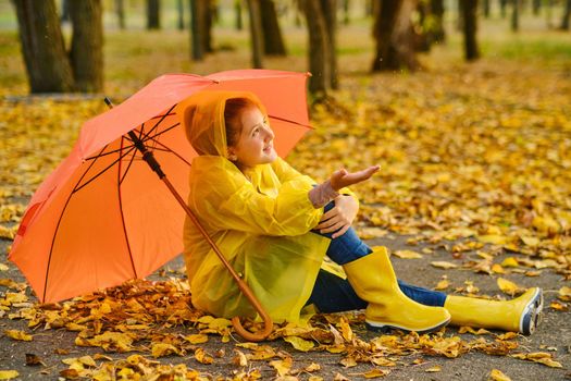 Happy kid Sits under an orange umbrella in the autumn park catching rain drops