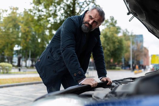 a man is trying to figure out the breakdown of the car standing at the open hood.