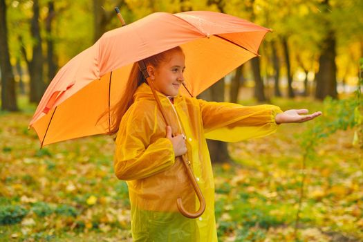 Happy child in the rain. Funny kid playing outdoors and catching rain drops in Autumn park