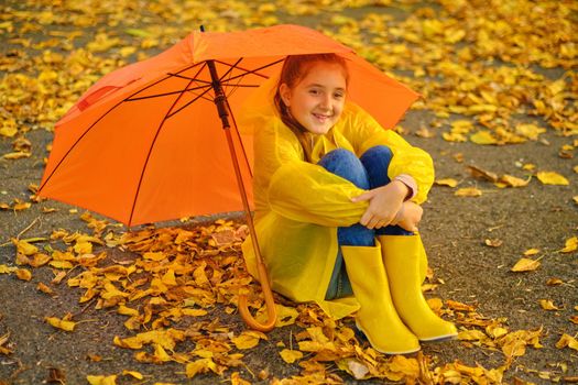 Happy kid Sits under an orange umbrella in the autumn park