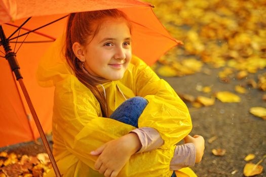 Happy kid Sits under an orange umbrella in the autumn park