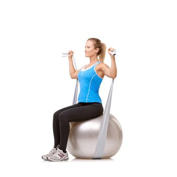 Total-body toning. A young woman sitting on an exercise ball while pulling a resistance band - profile