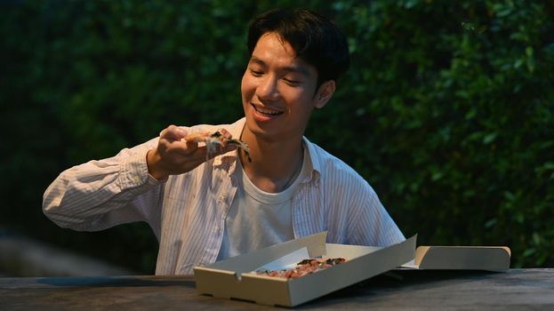 Happy young man eating eating pizza at outdoor at night market. Nightlife concept.