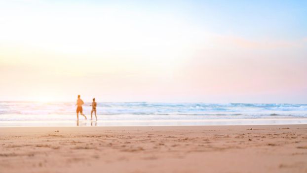 Couple running on the beach. Happy couple go to swim in ocean at sunset. Blurred summer vacation background. Defocused man and woman run on sandy sea beach. Summertime. Happy people