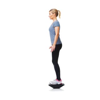 Balancing on her bosu - Health Fitness. A pretty young blond standing on a balance board while isolated on white