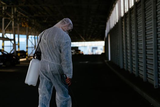 Worker wearing protective suit disinfection gear disinfect surface public place parking. Side view of disinfector safety overall and respiratory mask Covid pandemic disinfection preventive measures