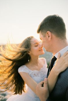 Bride with flowing hair almost kisses groom, putting her hand on his shoulder. High quality photo