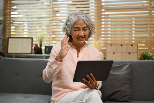 Smiling middle age woman having a video call with friends or family on digital tablet. People and communication concept.