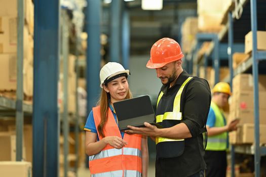 Warehouse workers wearing safety hardhat working on retail warehouse full of packed boxes and goods.