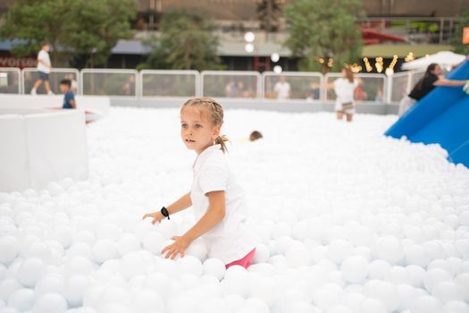 Happy little girl playing white plastic balls pool in amusement park. playground for kids. Active leisure for children.