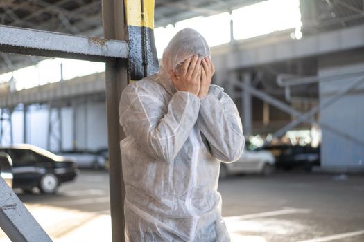 Despair healthcare worker in white covid protective overalls.Tired Male caucasian doctor grabs his head cower in depression during coronavirus pandemic Paramedic overworked cry covered face with hands