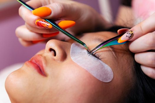 beautician applying eyelash extensions with tweezers to a beautiful young woman, concept of beauty and wellness