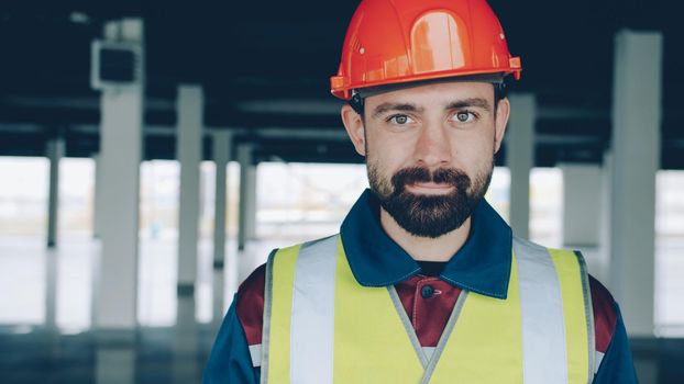 portrait of builder in uniform looking at camera and nodding head smiling standing indoors in plant. People and job concept.