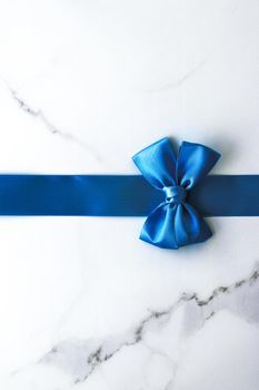 Happy holidays, festive decoration and brand sale promotion concept - Blue silk ribbon and bow on luxury marble background, holiday flatlay backdrop