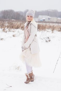 A blonde girl in winter clothes, walking on a snowy steppe. Smiling woman in light clothes in winter in the snow.