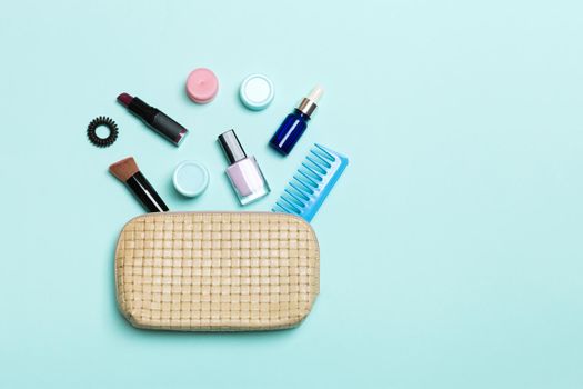 Top view of set of make up and skin care products spilling out of cosmetics bag on blue background. Beauty concept.