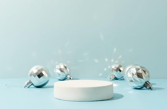 A minimalistic scene of a podium with christmas decorative balls on a light blue background. Catwalk for the presentation of products and cosmetics. Showcase with a stage for products, mockup design, seasonal