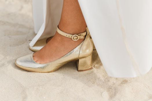 The golden shiny shoes of the bride on white sand on the ocean coast