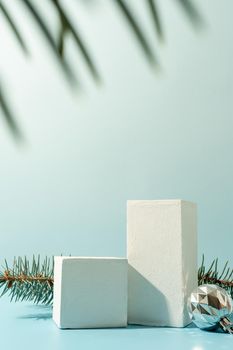 A minimalistic scene of podiums with christmas decorative balls and pine tree on a light blue background. Catwalk for the presentation of products and cosmetics. Showcase with a stage for products, mockup design, seasonal