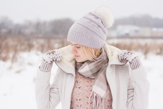 A blonde girl in winter clothes, walking on a snowy steppe. Smiling woman in light clothes in winter in the snow.