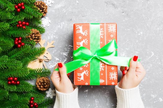 Top view of female hand tie up New Year present on festive wooden background. Fir tree and holiday decorations. Christmas time concept.