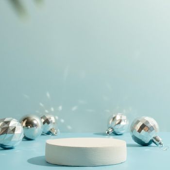 A minimalistic scene of a podium with christmas decorative balls and pine tree on a light blue background. Catwalk for the presentation of products and cosmetics. Showcase with a stage for products, mockup design, seasonal